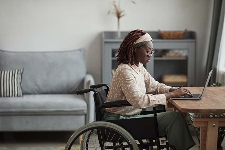 Side view portrait of young African-American woman using wheelchair while working from home in minimal grey interior, copy space